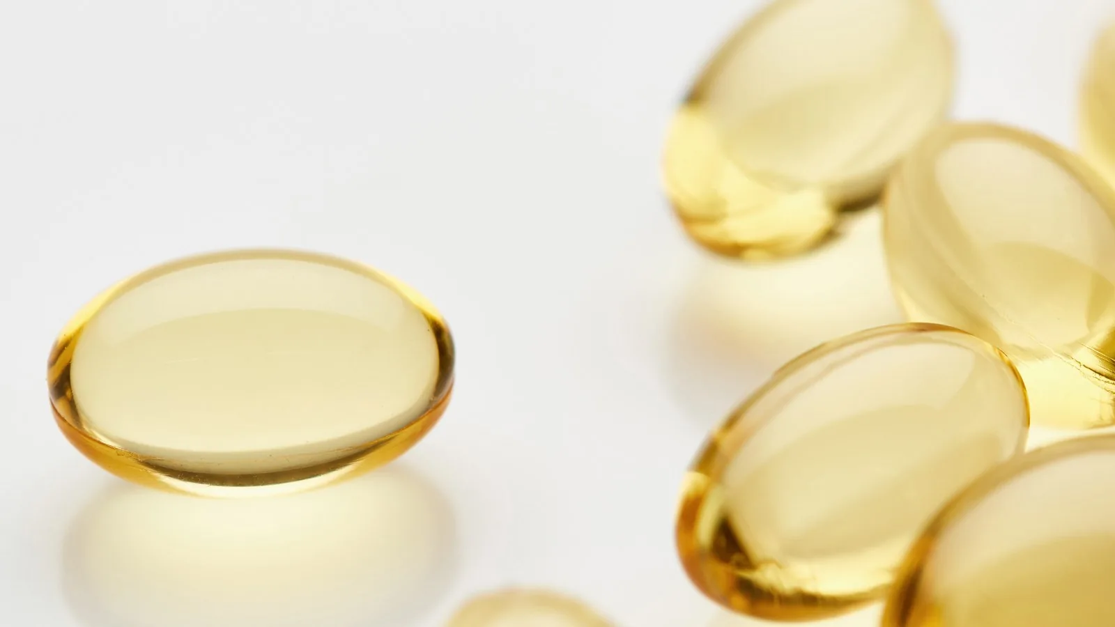 Golden omega-3 softgel capsules scattered on a pale surface in soft light.