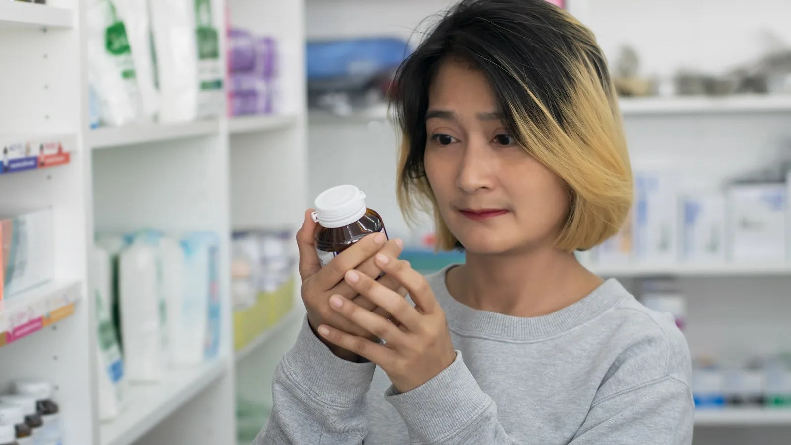 A shopper in a pharmacy aisle turning a supplement bottle over to read the label on the back.